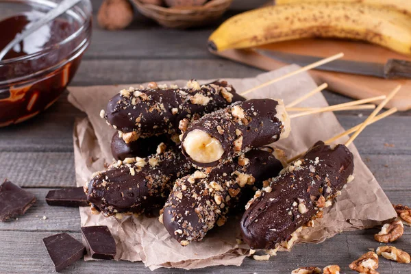 Frozen banana covered with chocolate and nuts on wooden rustic table