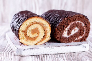 İki bisküvi. Çikolata ve beyaz kremalı sünger tahta kesme tahtasının üzerinde yuvarlanıyor.