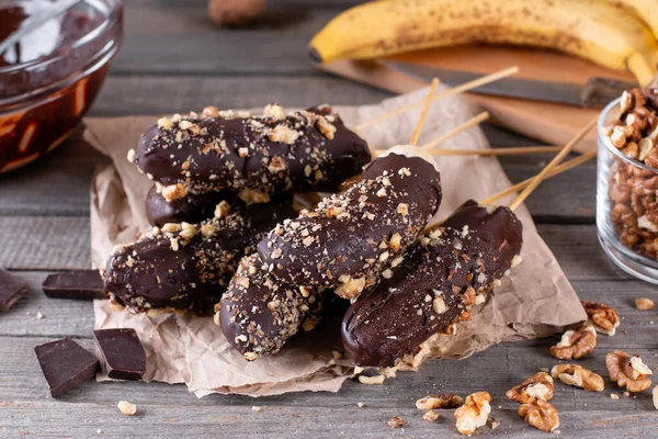Frozen banana covered with chocolate and nuts on wooden rustic table