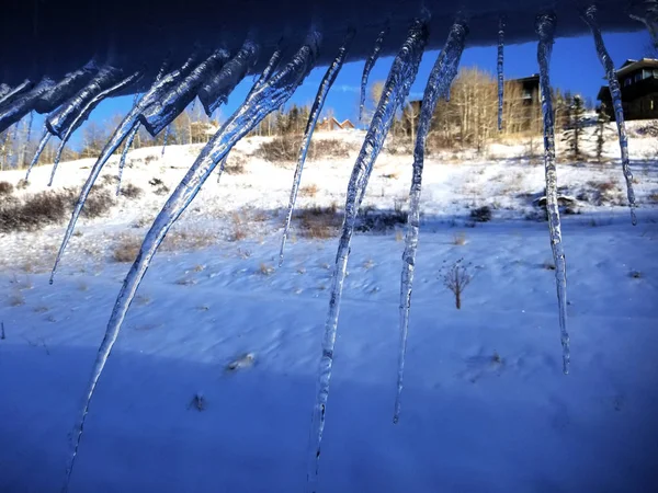 Hoekige ijspegels op een besneeuwde dakrand — Stockfoto