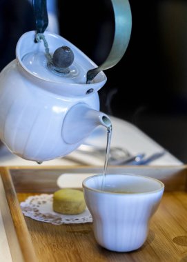 Beyaz çaydanlık çay fincanını bademli kurabiyeyle dolduruyor..