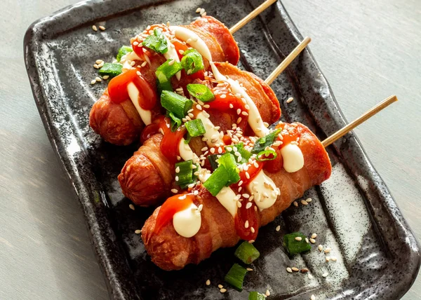 Pastırmalı sosisli sandviç. Üstü mayonez, ketçap, taze soğan, susam ve taze soğanla kaplı..