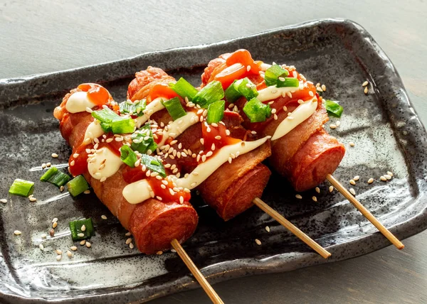 Pastırmalı sosisli sandviç. Üstü mayonez, ketçap, taze soğan, susam ve taze soğanla kaplı..