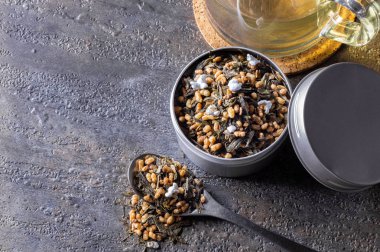 Organik ve doğal kahverengi pirinç çayı, kabın içinde genmaicha. Yanında da gri arka planda bir fincan sıcak çay..