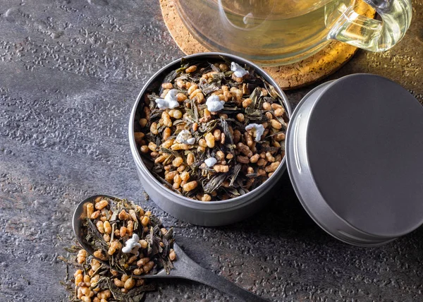 Organik ve doğal kahverengi pirinç çayı, kabın içinde genmaicha. Yanında da gri arka planda bir fincan sıcak çay..