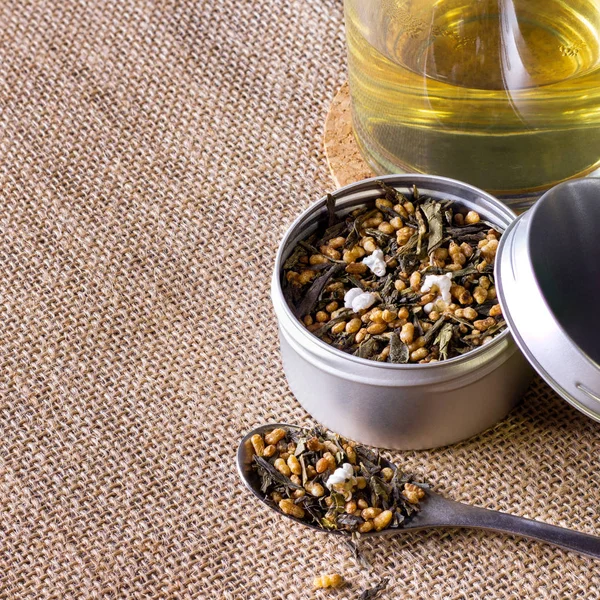 Organik ve doğal kahverengi pirinç çayı, kabın içinde genmaicha. Kahverengi arka planda bir fincan sıcak çay eşliğinde..