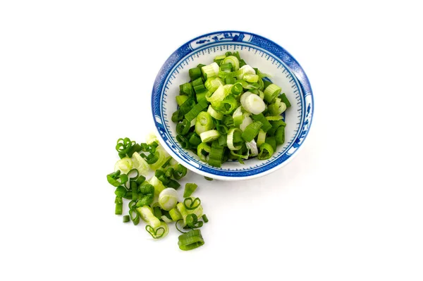 Doğranmış taze soğan, soğan, beyaz arka planda mavi bir tabakta.