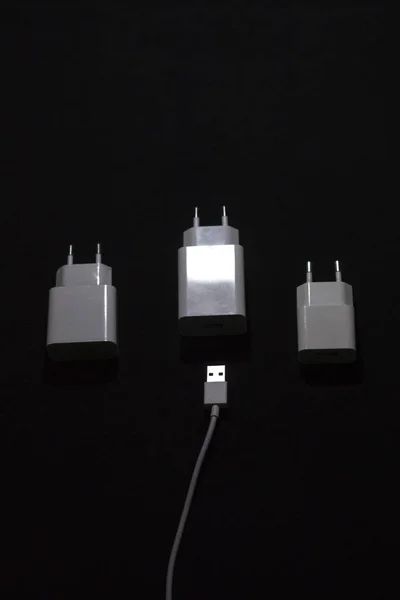 黒の背景に3つの白いスマートフォンの充電器 — ストック写真