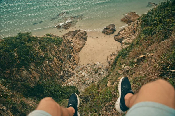 Young brave man sitting on a high stone cliff above ocean. Top view.