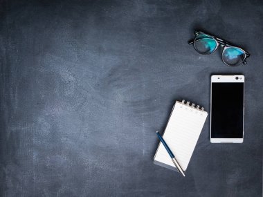 Telefon, gözlük ve karatahta kalemli defter.