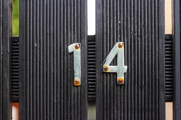 14 numaralı gümüş metal haneli ev, biraz paslı, siyah ahşap bir çit ya da kapı üzerinde.