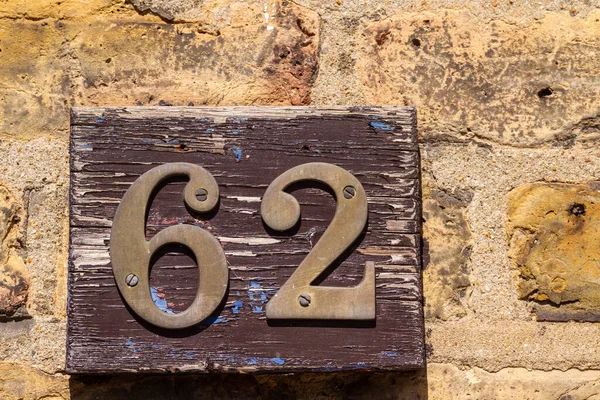 62 numaralı ev tuğla bir duvarda tahta bir plakette.