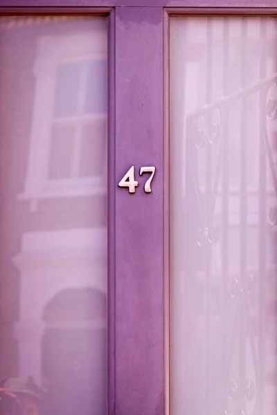 47 numaralı soluk mor ahşap ön kapıda büyük cam pencereli ve karşıdaki evi yansıtan bir ev.