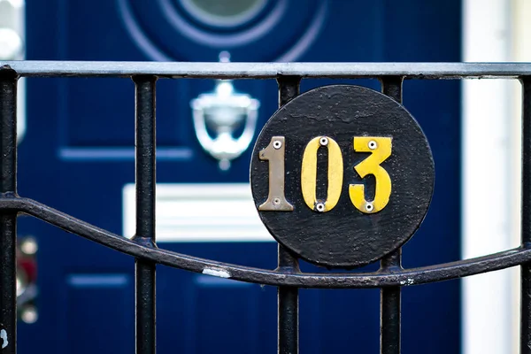 House number 103 on a round plaque in front of a blue wooden front door