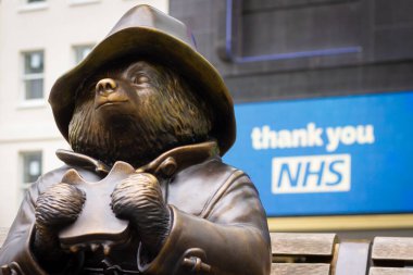 Londra, İngiltere - 15 Mayıs 2020: Bir Paddington Bear heykeli Leicester Meydanı 'nda bir teşekkür NHS tabelasının önünde sandviç yiyor.