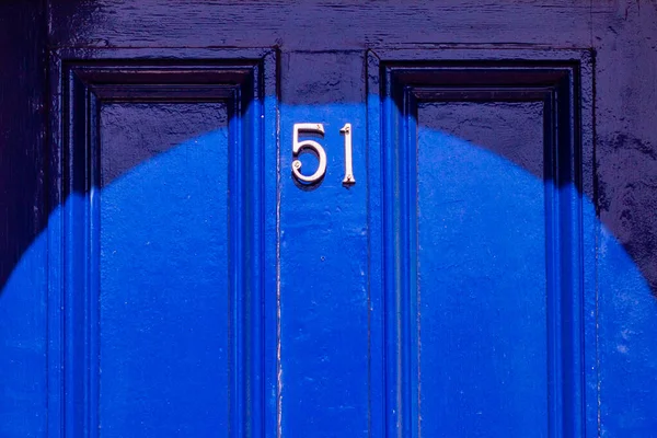 House number 51 on a royal blue wooden front door with vertical lines in London 