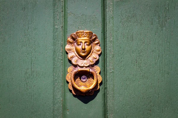 Bronze door knocker in the shape of a female head with peephole on a dark green wooden front door in London