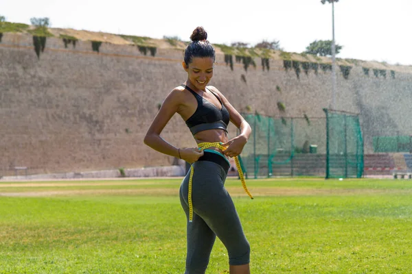 Female water sprinkled athlete in sportswear measuring waistline