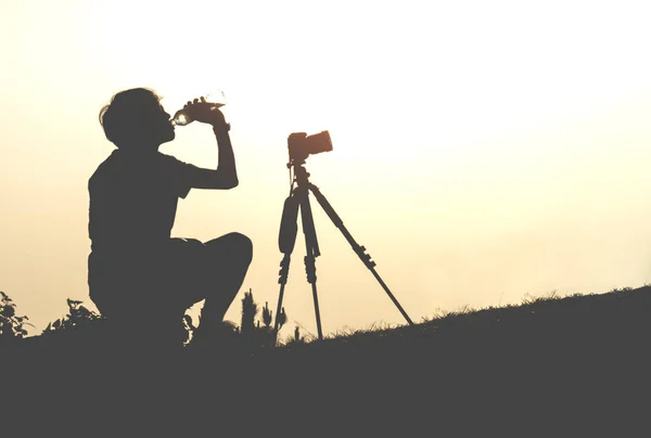 Silhouet toeristische man zit op de piek van de berg en drinken — Stockfoto