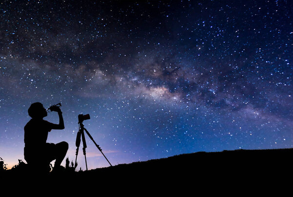 silhouette of tourist sitting and drinking on peak of mountain w