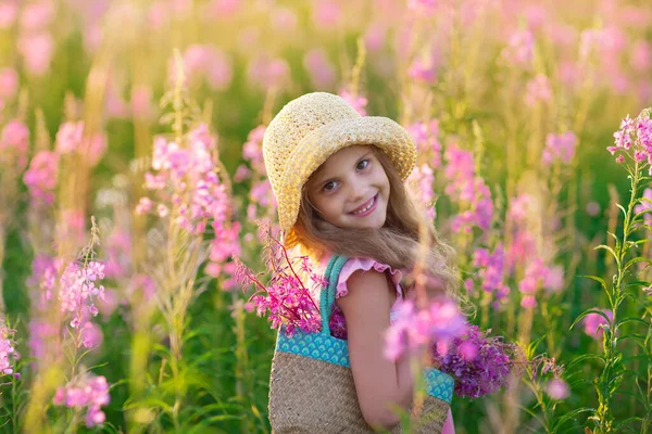 Küçük bir kız pembe tarlada gülümsüyor.