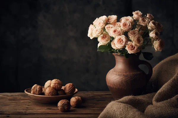 Still life with light roses and walnuts on wooden table with sacking