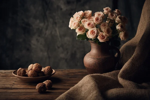 Still life with light roses and walnuts on the table with brown sacking