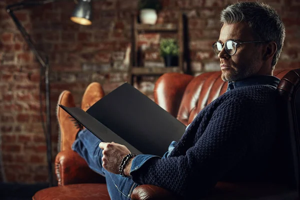Серьезный современный привлекательный мужчина с седыми волосами на чердаке студии с книгой в руках — стоковое фото