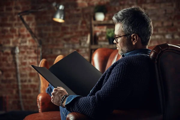 Sério moderno atraente homem com cabelos grisalhos no estúdio loft lendo um livro — Fotografia de Stock