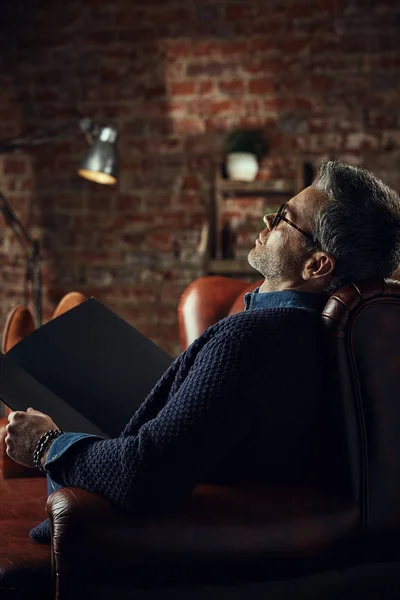 Elegante hombre atractivo con pelo gris en el estudio loft con un libro en sus manos — Foto de Stock