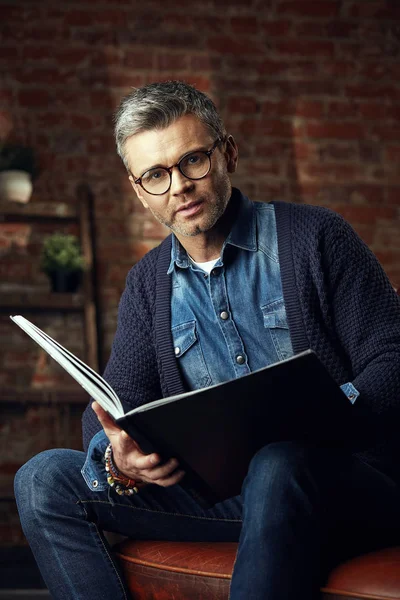 Potret pria tampan berkacamata dengan rambut abu-abu di loteng studio dengan sebuah buku — Stok Foto
