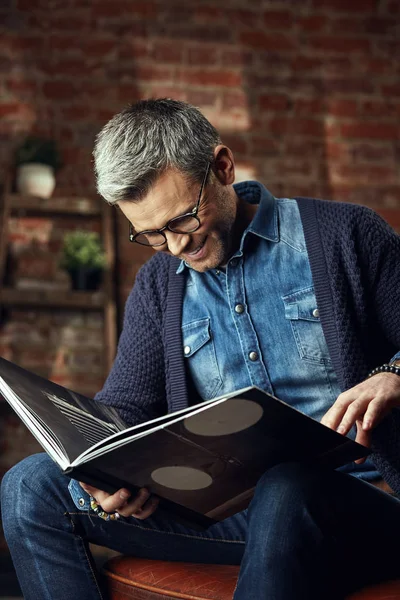 Retrato de hombre atractivo en gafas con pelo gris en estudio loft leyendo un libro — Foto de Stock