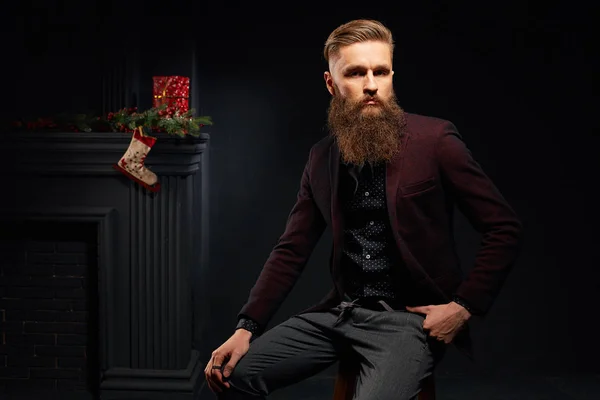 Bello uomo elegante seduto in studio scuro con calza di Natale sullo sfondo — Foto Stock