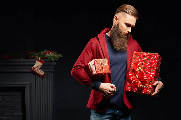빨간 크리스마스 스튜디오에 잘생긴 심각한 수염된 남자 그의 손에 상자 — 스톡 사진