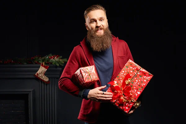 Young smiling man with long beard with red christmas boxes in his hands — Stock Photo, Image