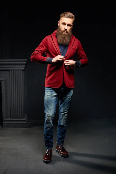 Attractive man with long beard in dark studio wearing red jacket — Stock Photo, Image