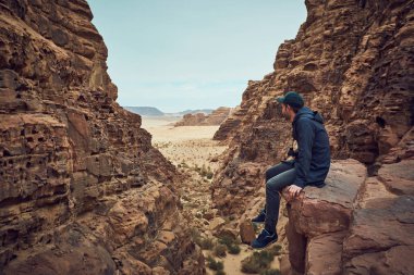 Wadi Rum çölde Ürdün kırmızı kayaya oturan karanlık giysili ciddi adam