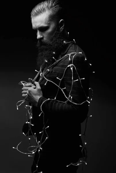 Портрет серйозного красивого чоловіка з бородою і різдвяними вогнями в студії в чорно-білому — стокове фото