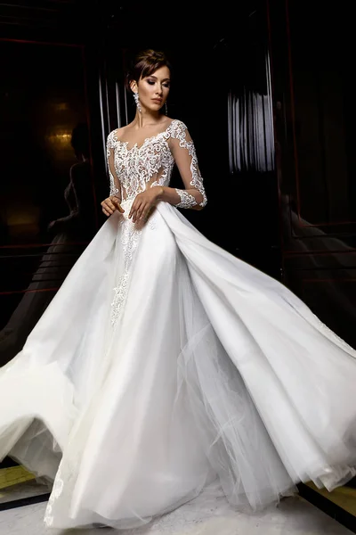 Young brunette model poses in long bridal dress with lace on fashion background — Stock Photo, Image