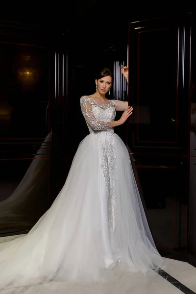 Attraktive junge brünette Modell posiert in langen Brautkleid mit Spitze auf Modehintergrund — Stockfoto