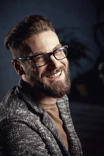 Крупный план портрета красивого улыбающегося милого мужчину с бородой в очках на тёмном фоне — стоковое фото