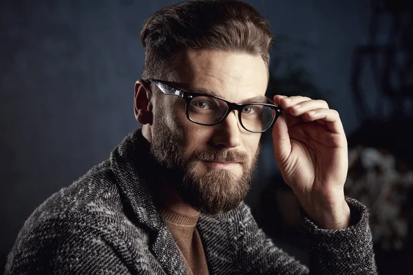 Nahaufnahme Porträt eines hübschen ernsthaften netten Mannes mit Bart in Brille auf dunklem Hintergrund — Stockfoto