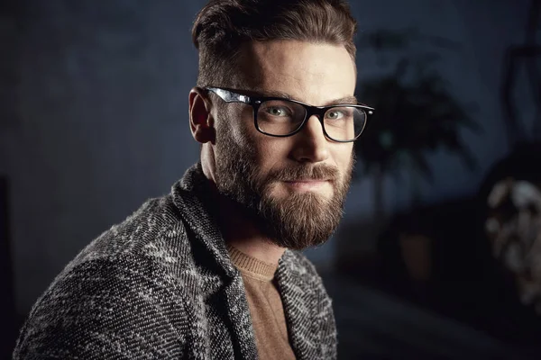 Closeup portrait of handsome serious cute man in grey with beard in glasses on dark background — Stock Photo, Image