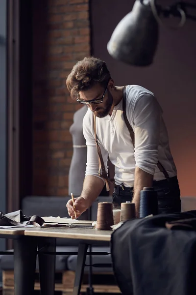 Fiatal komoly török szakáll és harisnyatartók dolgozik közelében csodálatos műtermében, antik bútorokkal és manöken szálak fából készült asztal háttere fehér ing szemüveg — Stock Fotó