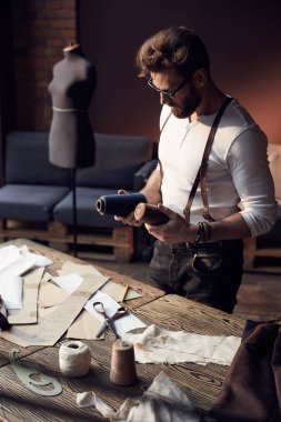 Sakal ve gözlük kahverengi deri jartiyer konu ve antika mobilyalar ve manken şaşırtıcı atelier makas ile ahşap masa yakınındaki arka plan üzerinde çalışma ile beyaz gömlek büyük ciddi terzi