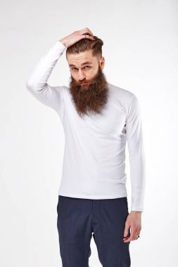 Young bearded man posing in studio in trendy white long-sleeve  shirt with print and blue chinos clipart