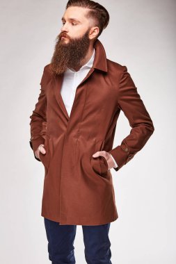 Genç adam Studio kahverengi uzun ceket ve Mavi pantolon ayakta sakallı