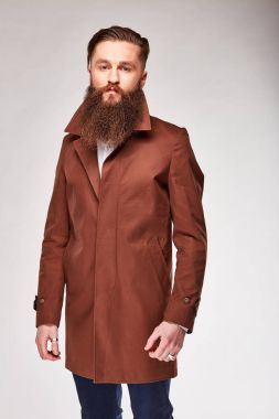 Genç adam Studio kahverengi uzun ceket ve Mavi pantolon poz sakallı