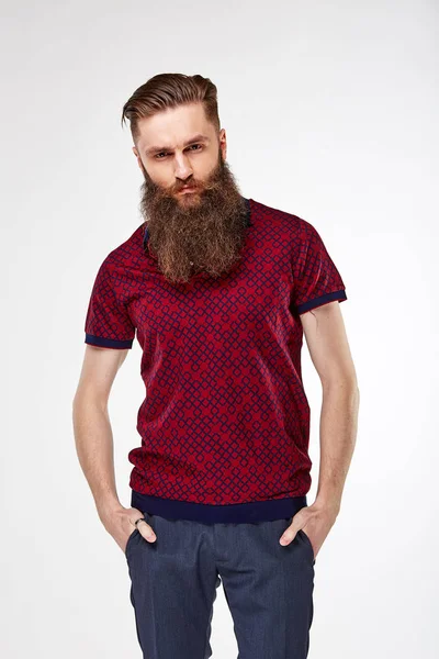 Молодой бородатый мужчина позирует в студии в модной темно-красной футболке с принтом и синими чино — стоковое фото