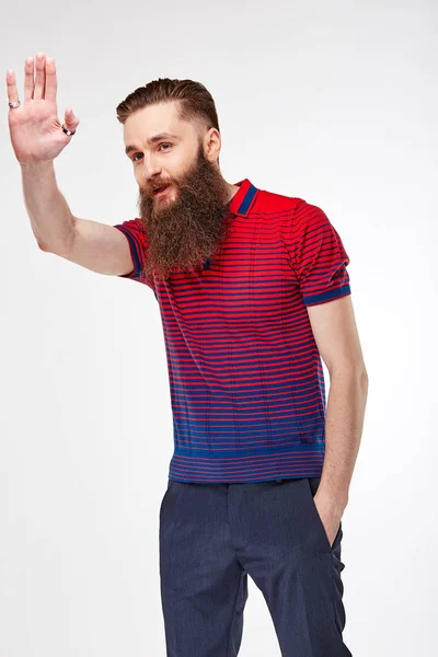Молодой бородатый мужчина позирует в студии в модной красно-синей футболке с полосками и синими чино — стоковое фото